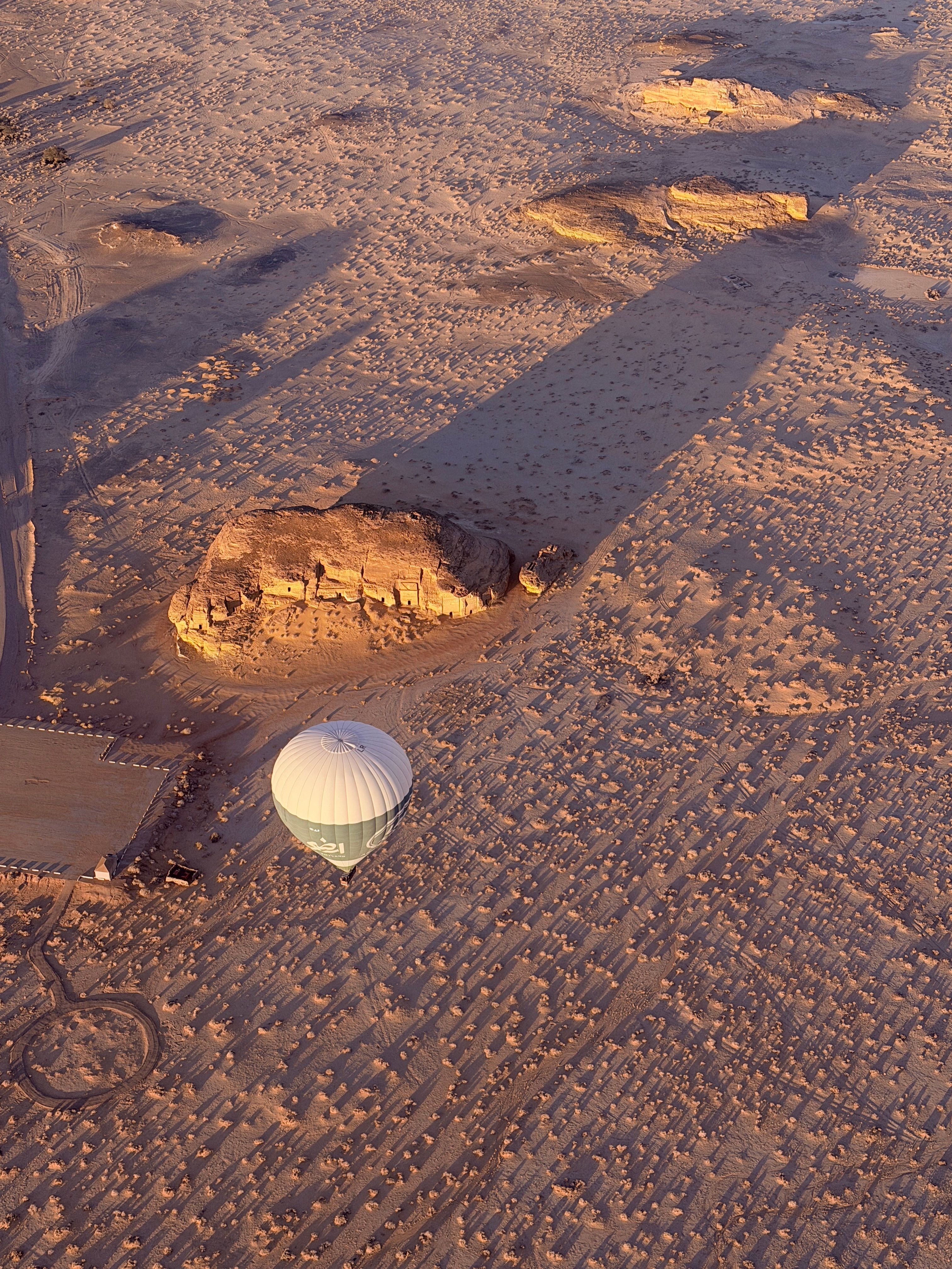 Aerial view of a hot air balloon casting its shadow over the ancient rock formations of AlUla desert, Saudi Arabia