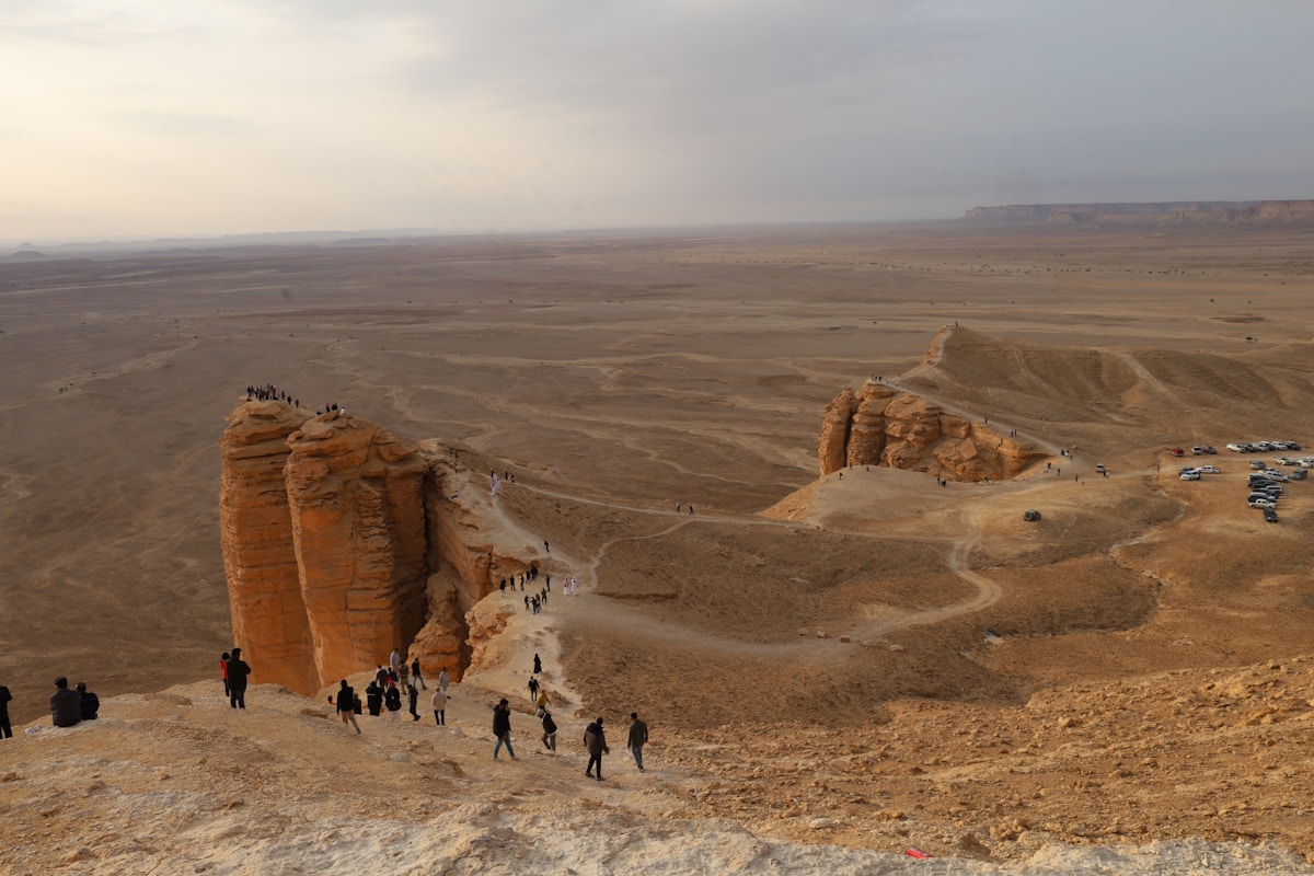 Hikers on the Edge of the World escarpment looking out over a vast Saudi Arabian desert plain