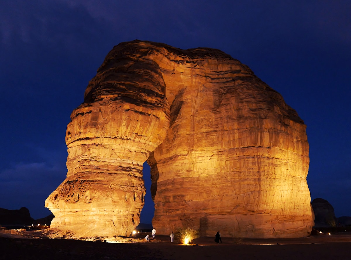 Large rock formation illuminated at night under a dark blue sky, AlUla, Saudi Arabia