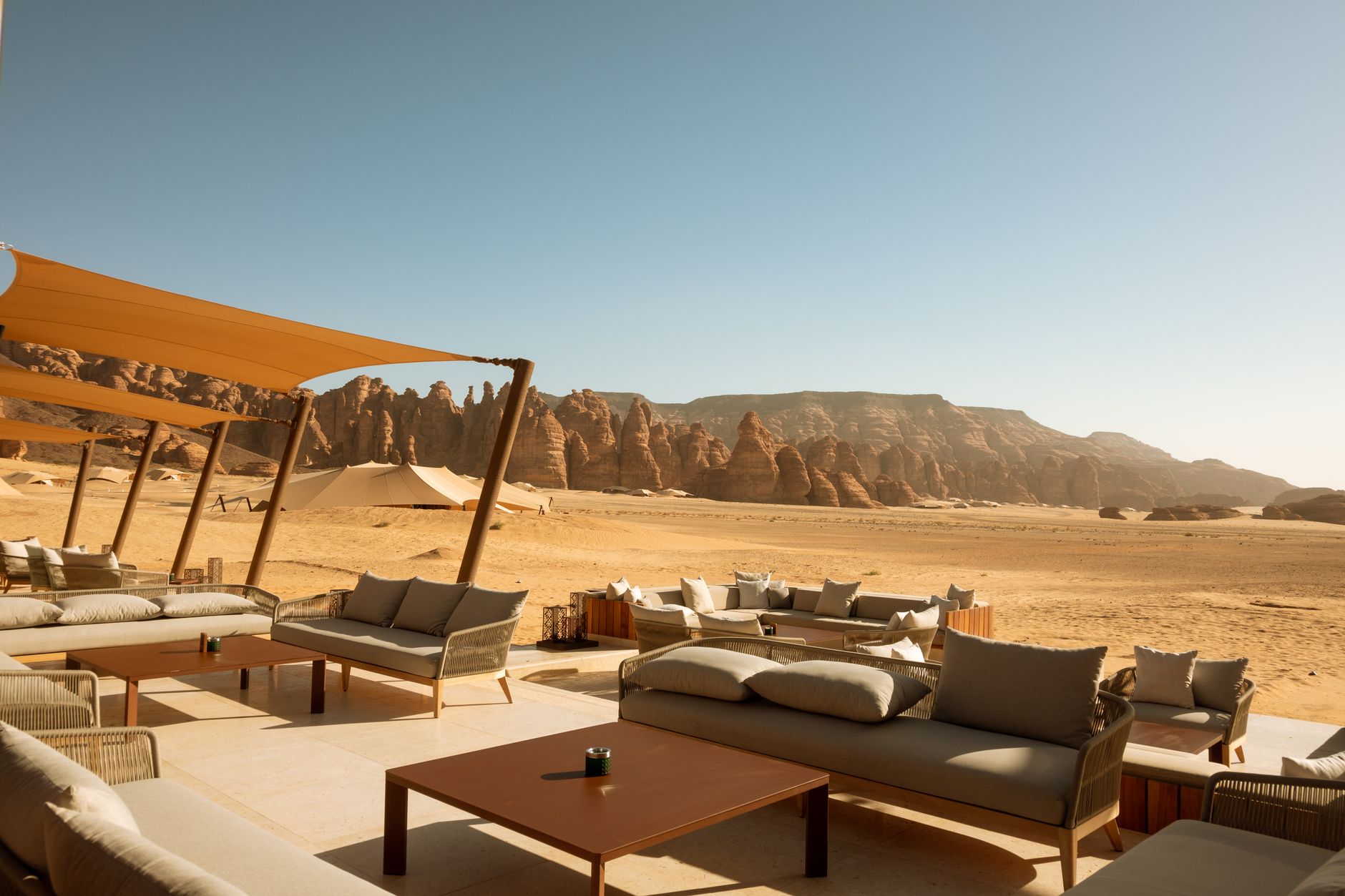 Luxury desert resort terrace with sofas and shade sails overlooking AlUla sandstone rock formations