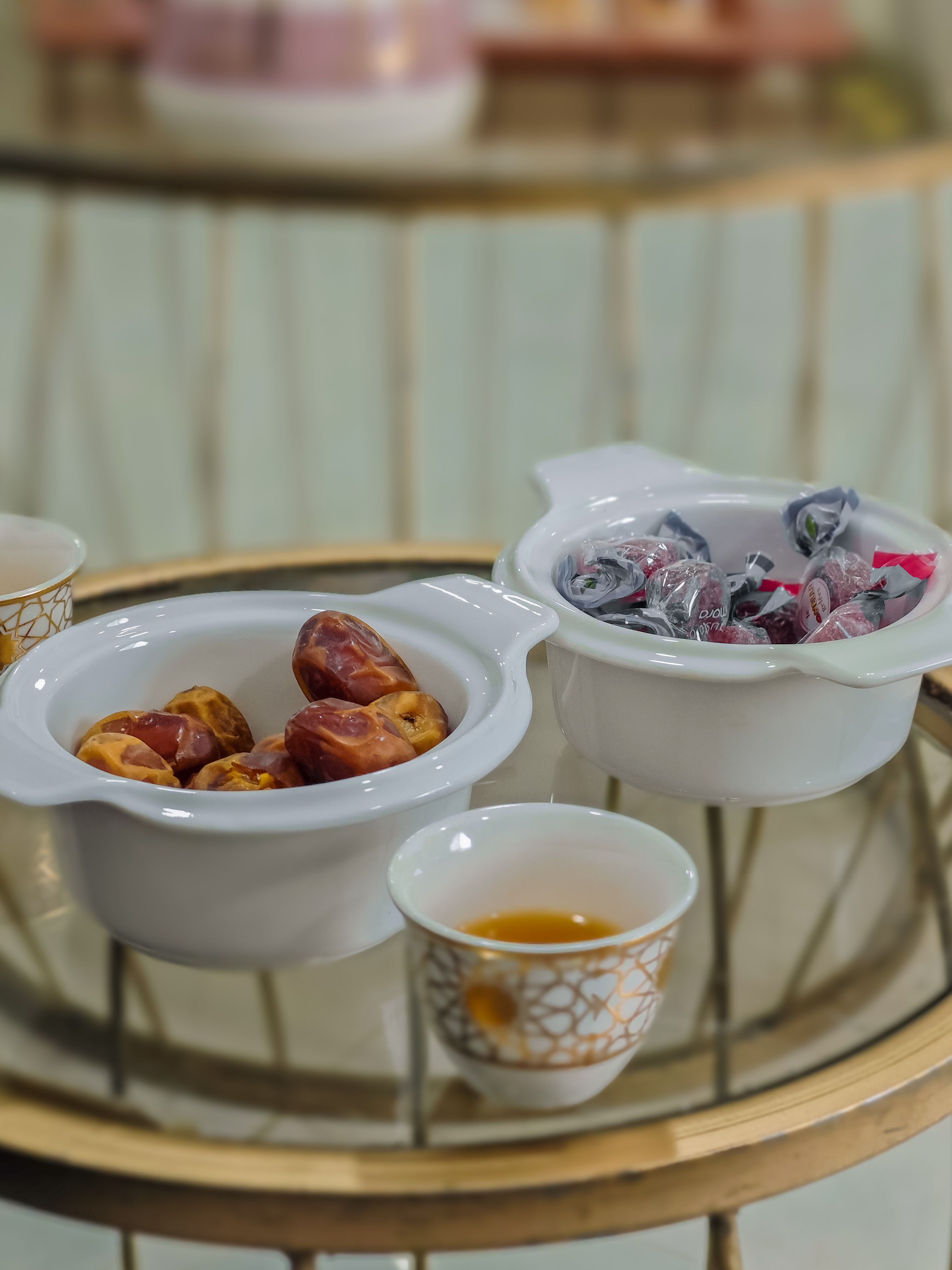 Traditional Arabic dates and sweets in white bowls alongside a qahwa coffee cup on a gilded tray
