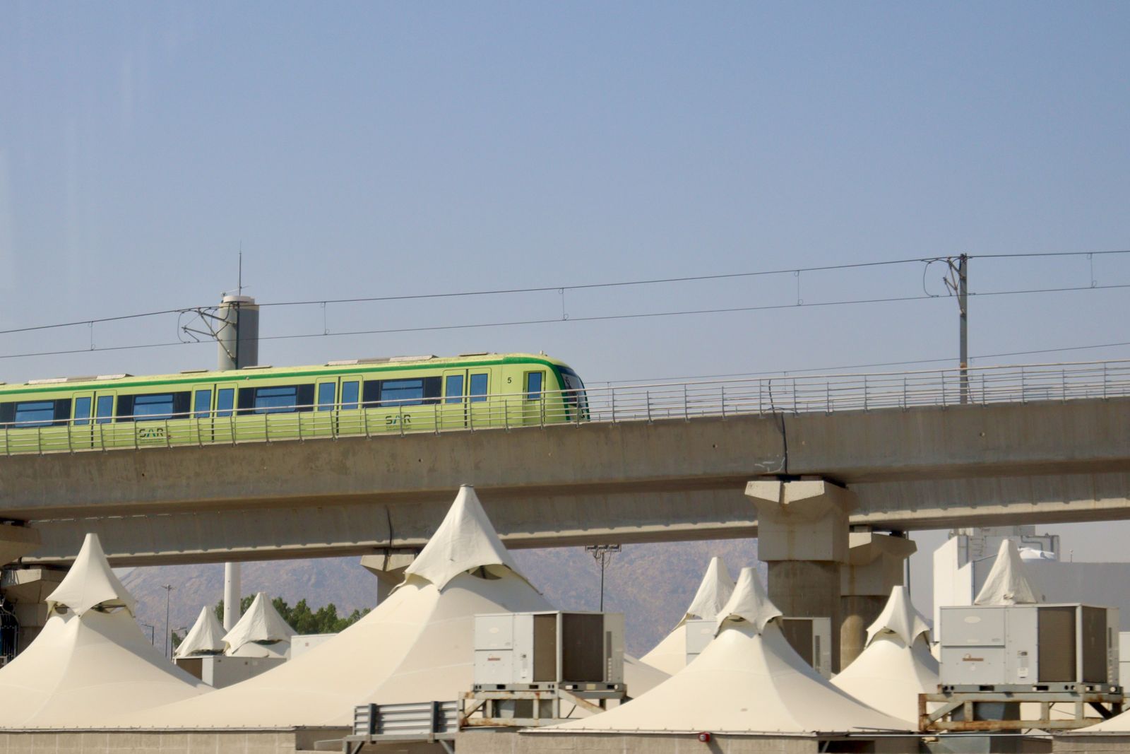 The green SAR Haramain High-Speed Railway train running on elevated tracks above the Hajj pilgrim camps near Makkah