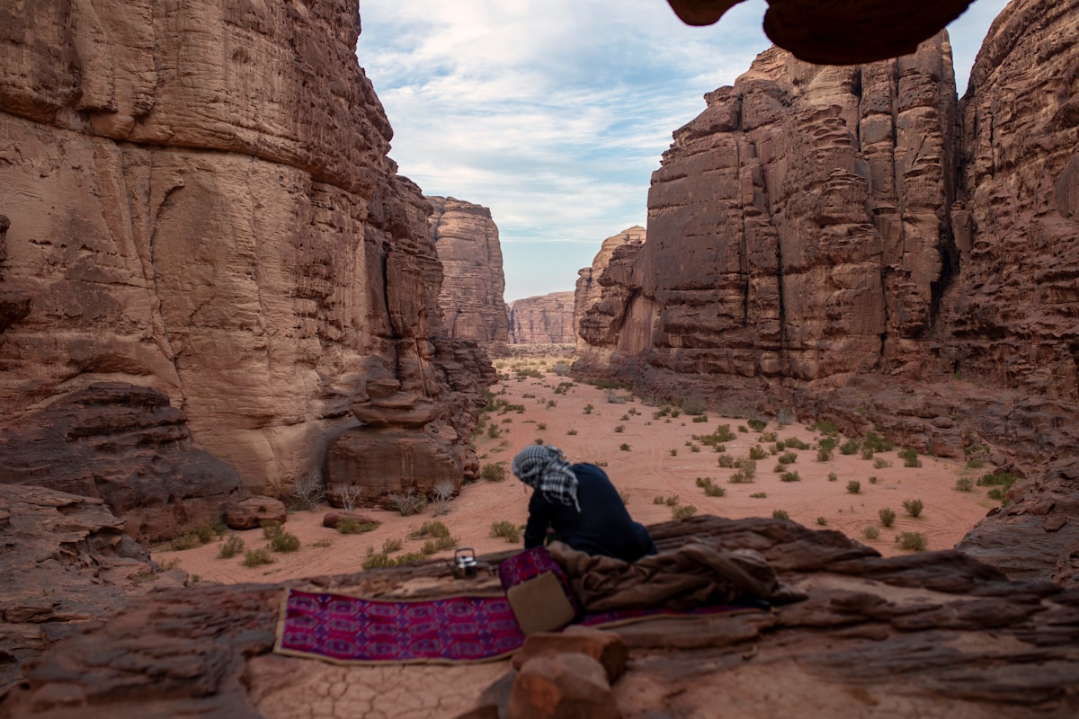 Man making tea beside a traditional rug in a red sandstone canyon in Tabuk, Saudi Arabia