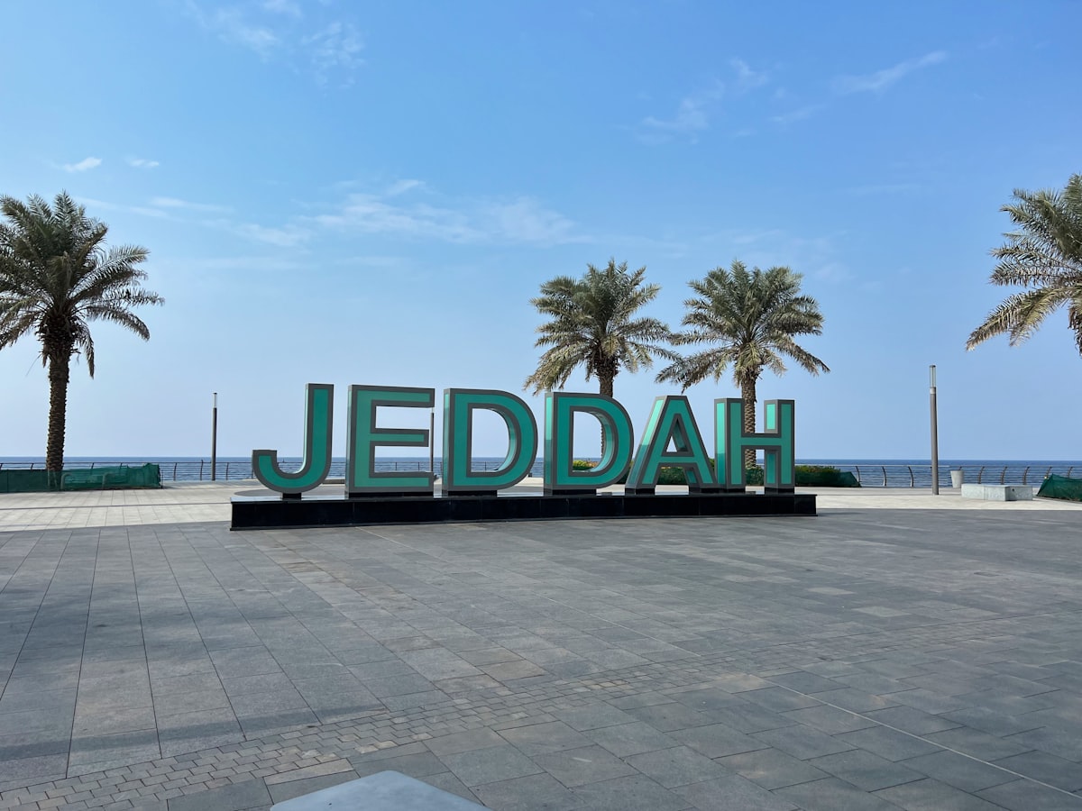 Jeddah sign on the Corniche waterfront with palm trees and the Red Sea behind