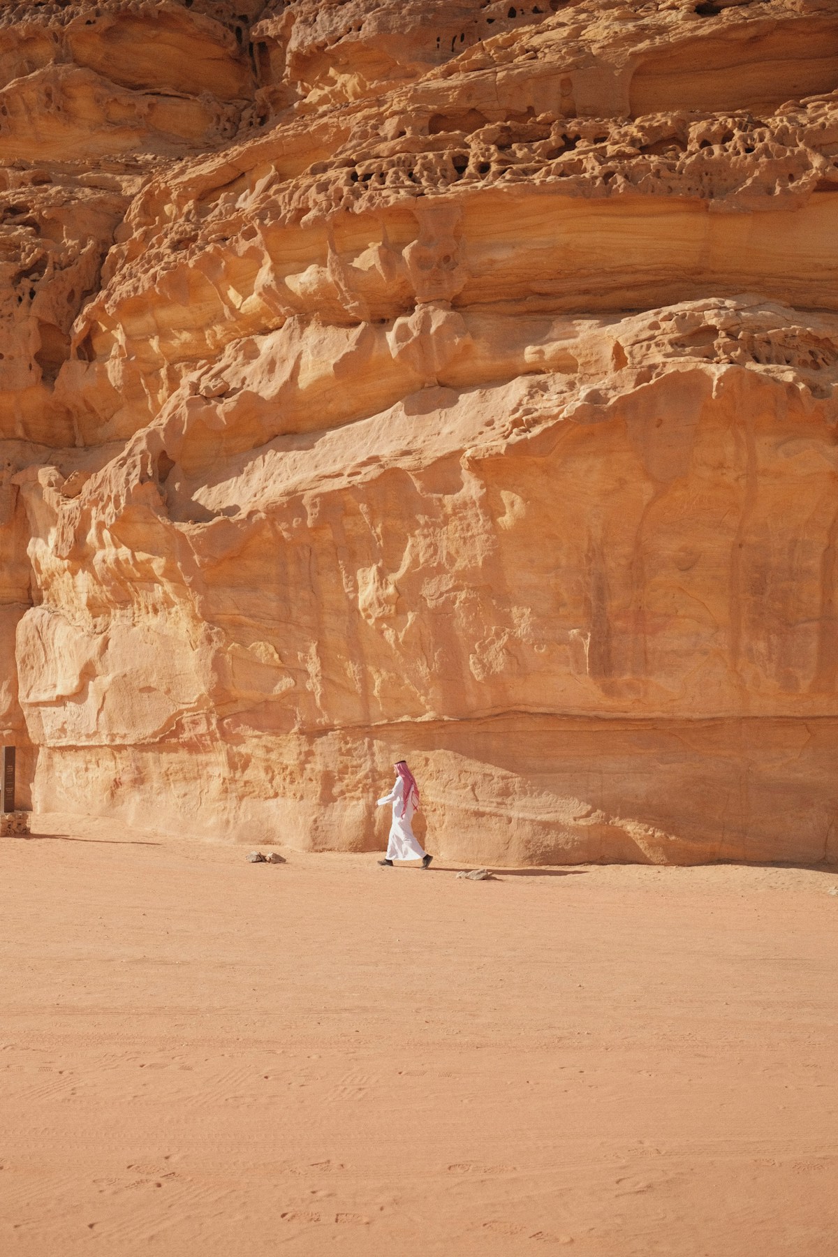 Man in traditional white thobe walking beside sandstone cliffs, AlUla desert, Saudi Arabia
